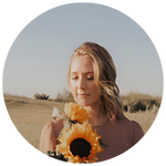 A woman holding a sunflower and gazing downward in a field.