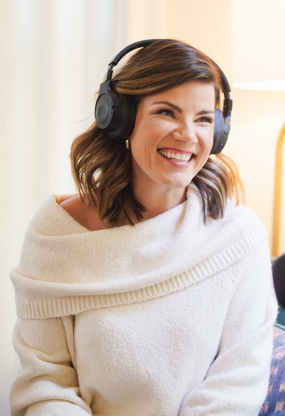 A smiling woman wearing an off-the-shoulder sweater and headphones.