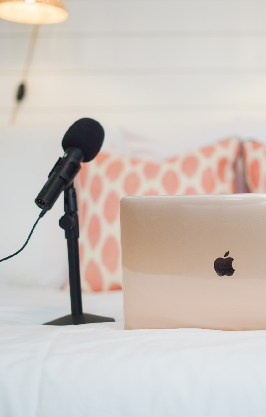 A microphone on a stand near an open laptop on a white bedspread.