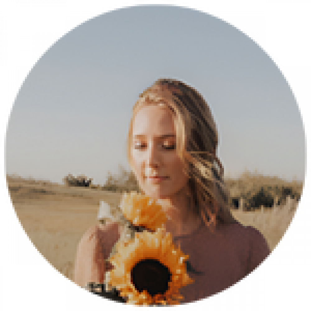 A woman holding a sunflower and gazing downward in a field.